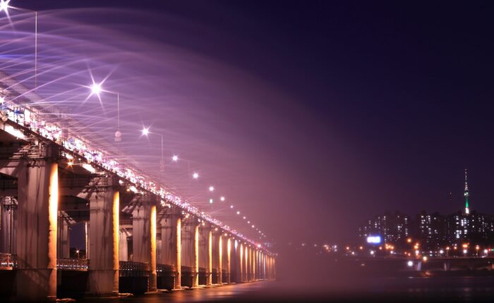 Night view of an illuminated bridge and city skyline, showcasing vibrant lights and urban architecture.