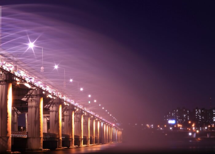 Night view of an illuminated bridge and city skyline, showcasing vibrant lights and urban architecture.