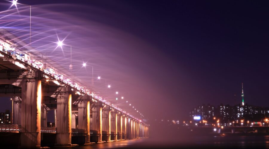 Night view of an illuminated bridge and city skyline, showcasing vibrant lights and urban architecture. 汉江野餐团, 盘浦汉江公园野餐垫, Some Sevit夜景, 彩虹喷泉表演, 便利店美食组合, 반포 한강공원 피크닉 매트, 세빛섬 야경, 무지개 분수 쇼, 편의점 꿀조합 미식, Han River Picnic Tour, Banpo Park picnic mat, Some Sevit night view, Rainbow Fountain show, convenience store spread, 盤浦漢江公園野餐墊, 漢江野餐團, 世貌島夜景, 彩虹噴泉表演, 便利商店美食組合