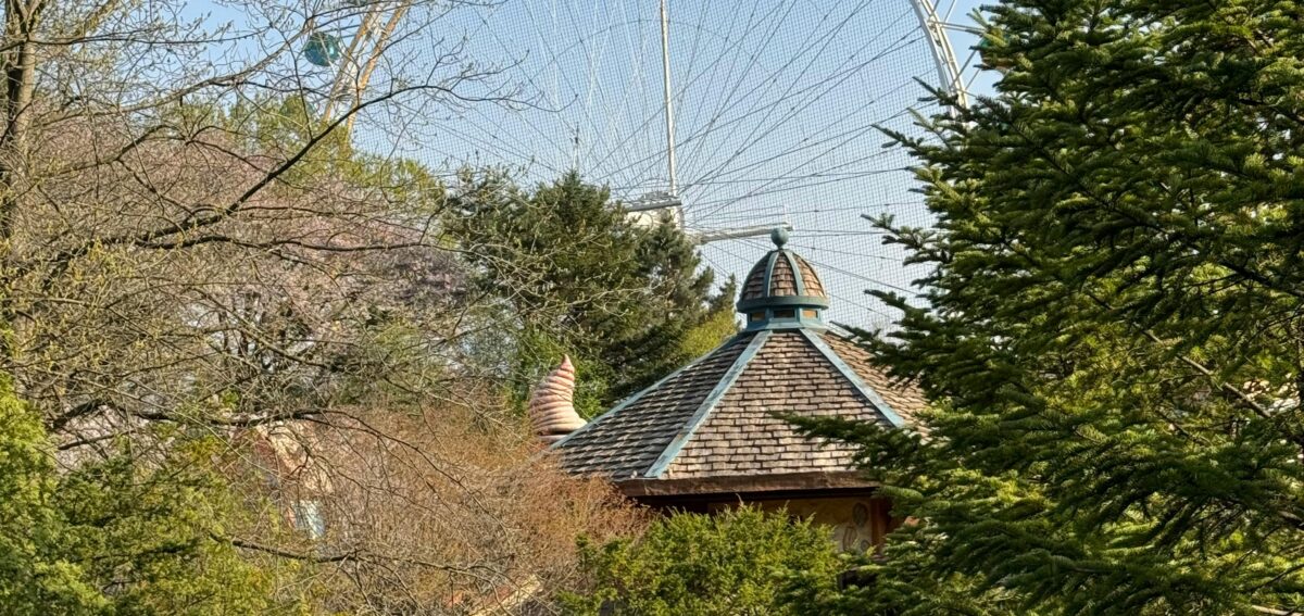 A stunning view of a Ferris wheel towering above lush greenery in a tranquil park setting.