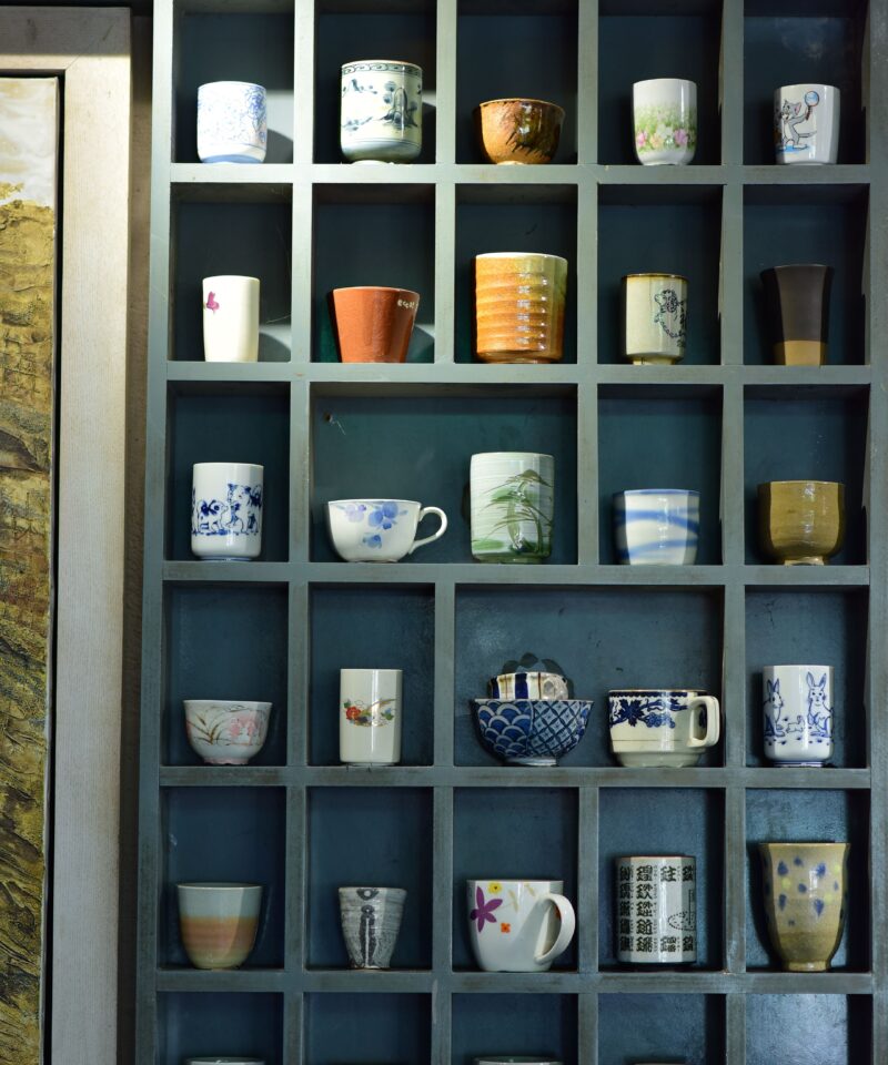 A variety of decorative ceramic cups and mugs arranged on a display shelf, showcasing diverse designs and colors.